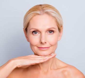 Pretty, attractive, charming, woman demonstrate, show, present her perfect skin after peeling, lotion, mask, isolated on grey background, holding hand under chin, treatment, therapy concept