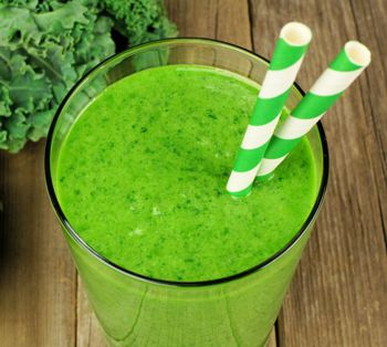 Healthy green kale smoothie in a glass with straws on wood background
